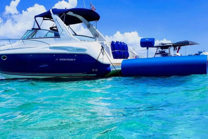 Blue and white boat floating on clear turquoise water with a sunny sky.