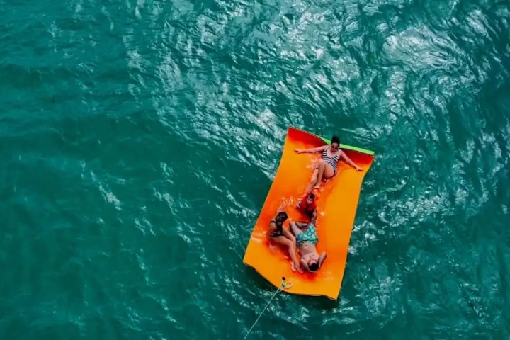 Four people relaxing on an orange float in blue water, viewed from above.