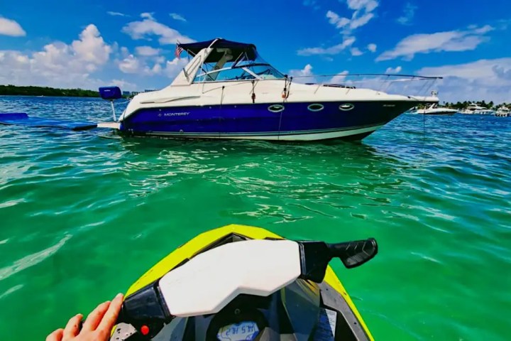View from jet ski approaching a boat on clear turquoise water under a blue sky.
