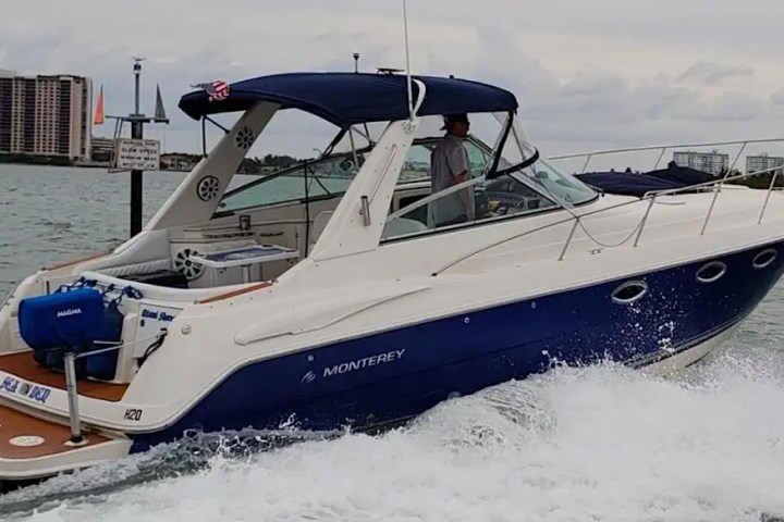 A blue and white motorboat speeds through water, with buildings visible in the background.