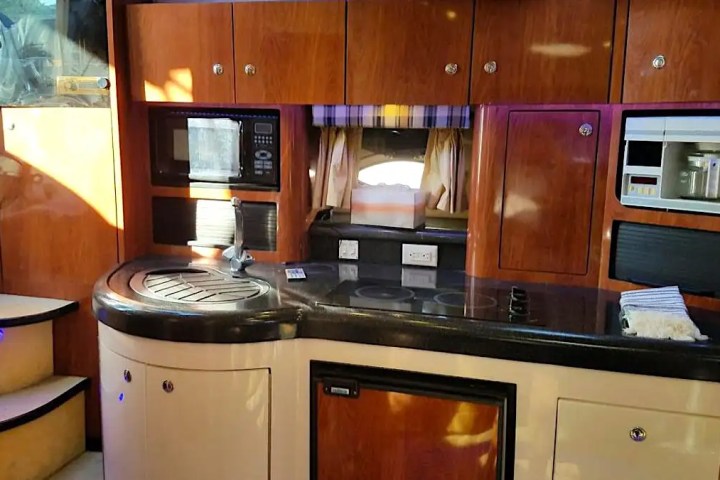 Boat interior with a kitchen, wooden cabinets, stove, sink, microwave, and steps.