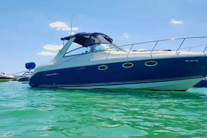 Blue and white motorboat floating on calm water under a clear sky.