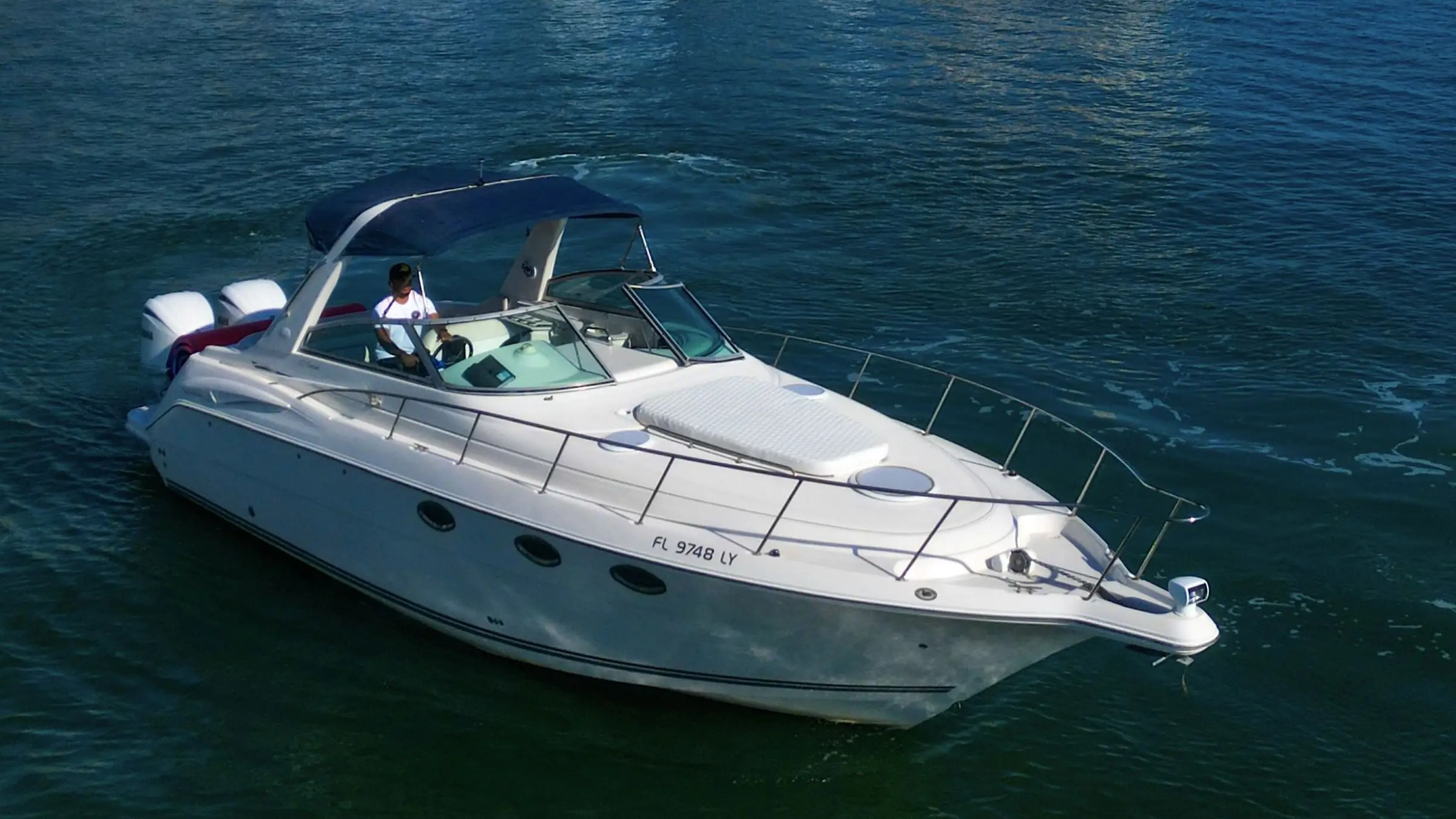 White motorboat with two engines on blue water, person at the helm, sunny weather.