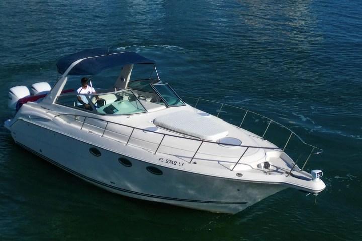 White motorboat with two engines on blue water, person at the helm, sunny weather.