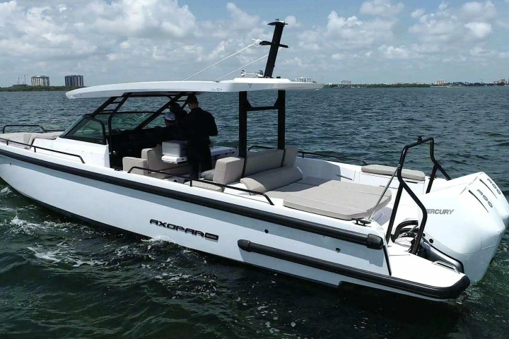 White motorboat with a roof on water, city skyline visible in background.
