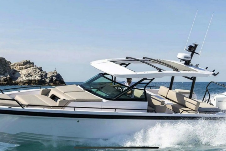 A luxury motorboat sailing on the sea near rocky cliffs under a clear sky.