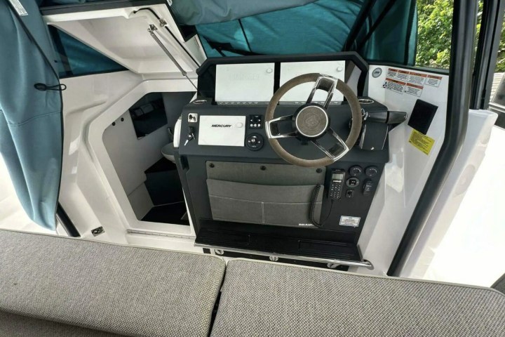 Boat cockpit with steering wheel, instrument panel, and open cabin door, featuring cushioned seating.
