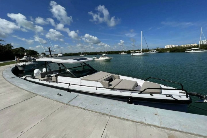 Moored modern boat by a pier under blue sky with distant sailboats on the water.