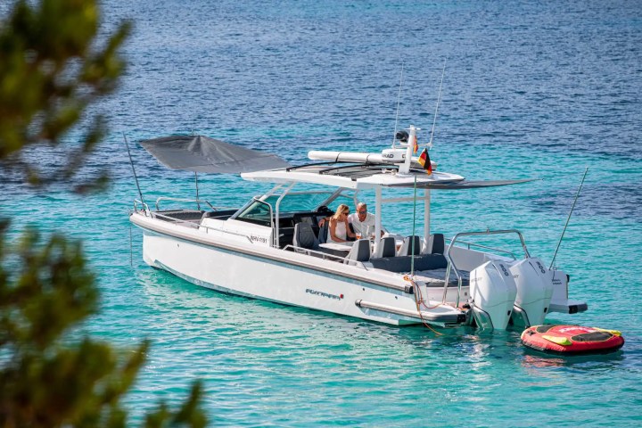 Motorboat with two people floats on turquoise water, surrounded by trees.