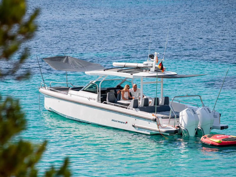 Motorboat with two people floats on turquoise water, surrounded by trees.