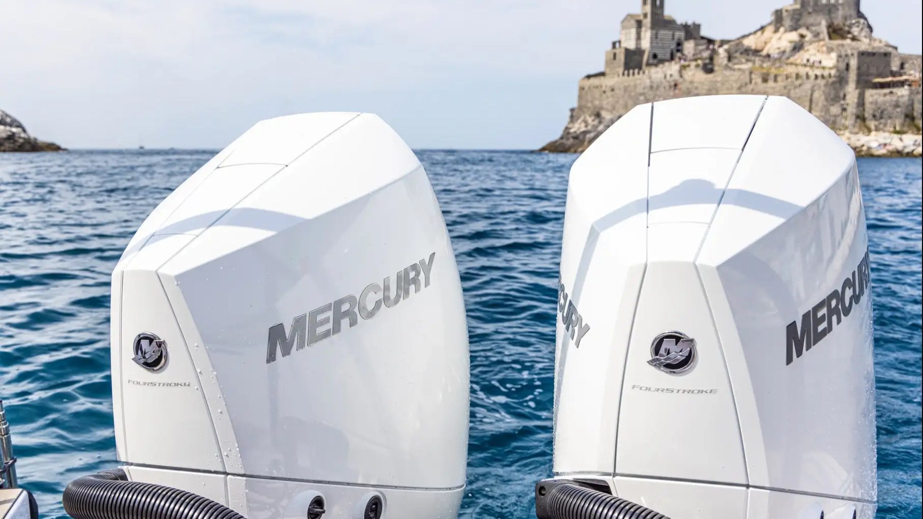 Two Mercury boat engines with a seaside castle in the background.