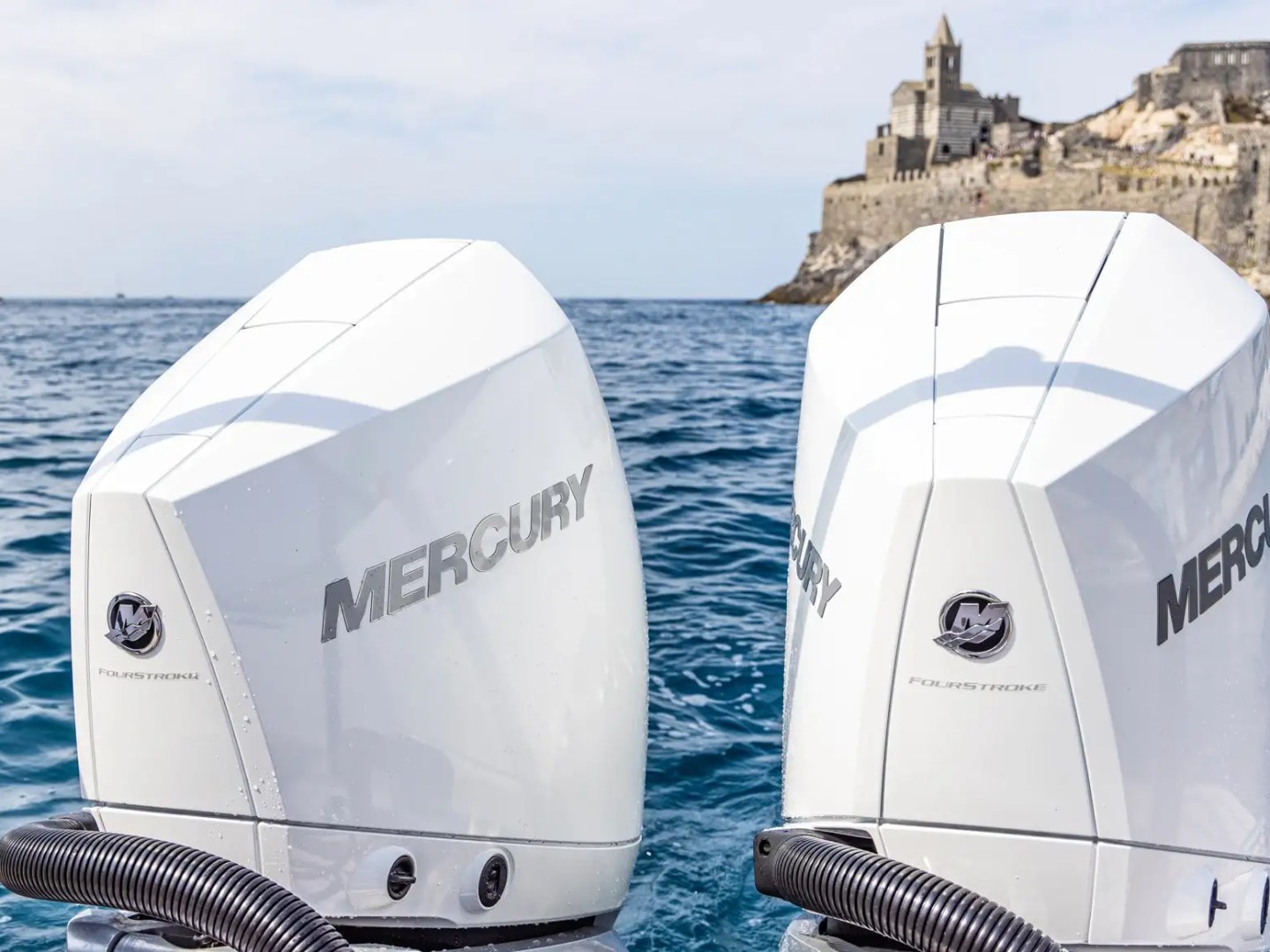 Two Mercury boat engines with a seaside castle in the background.