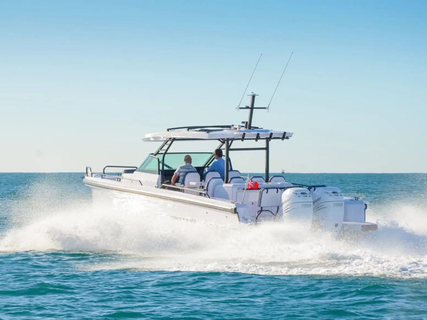 A motorboat speeding across the ocean under a clear blue sky.
