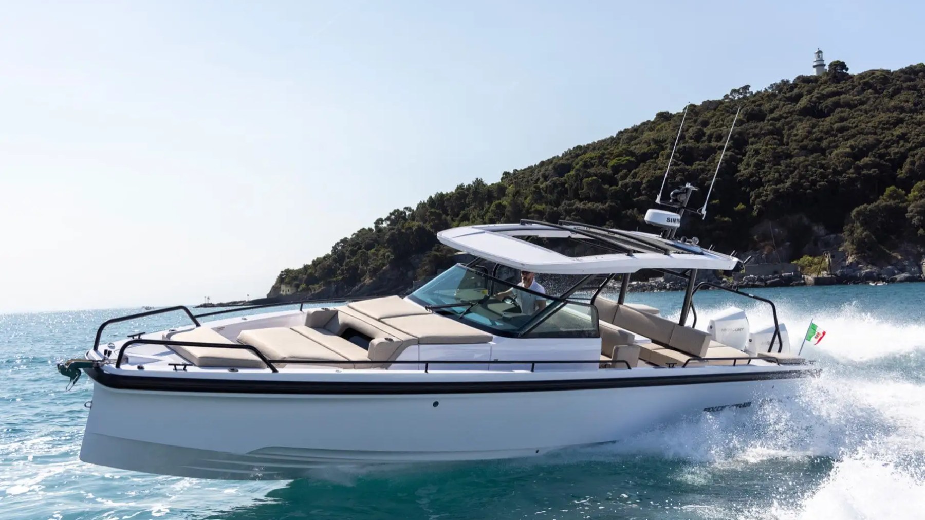 Speedboat cruising on sea with distant hillside and small lighthouse in background.