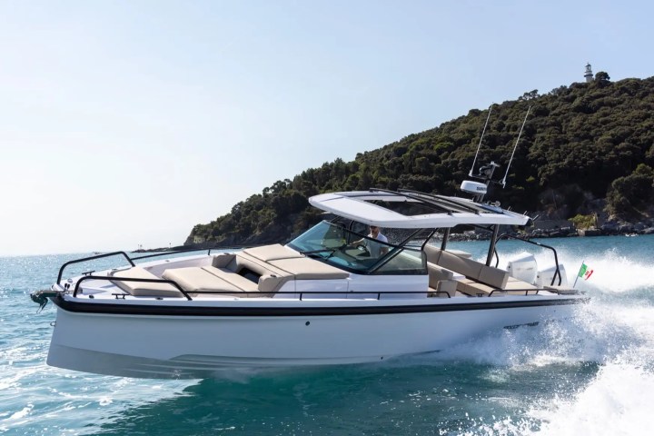 Speedboat cruising on sea with distant hillside and small lighthouse in background.