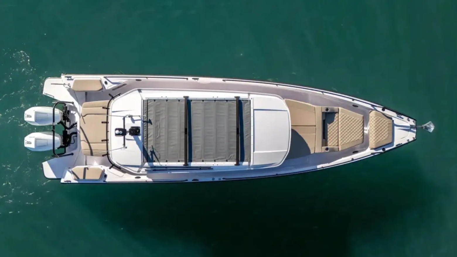 Top view of a sleek motorboat with dual engines on a calm green sea.