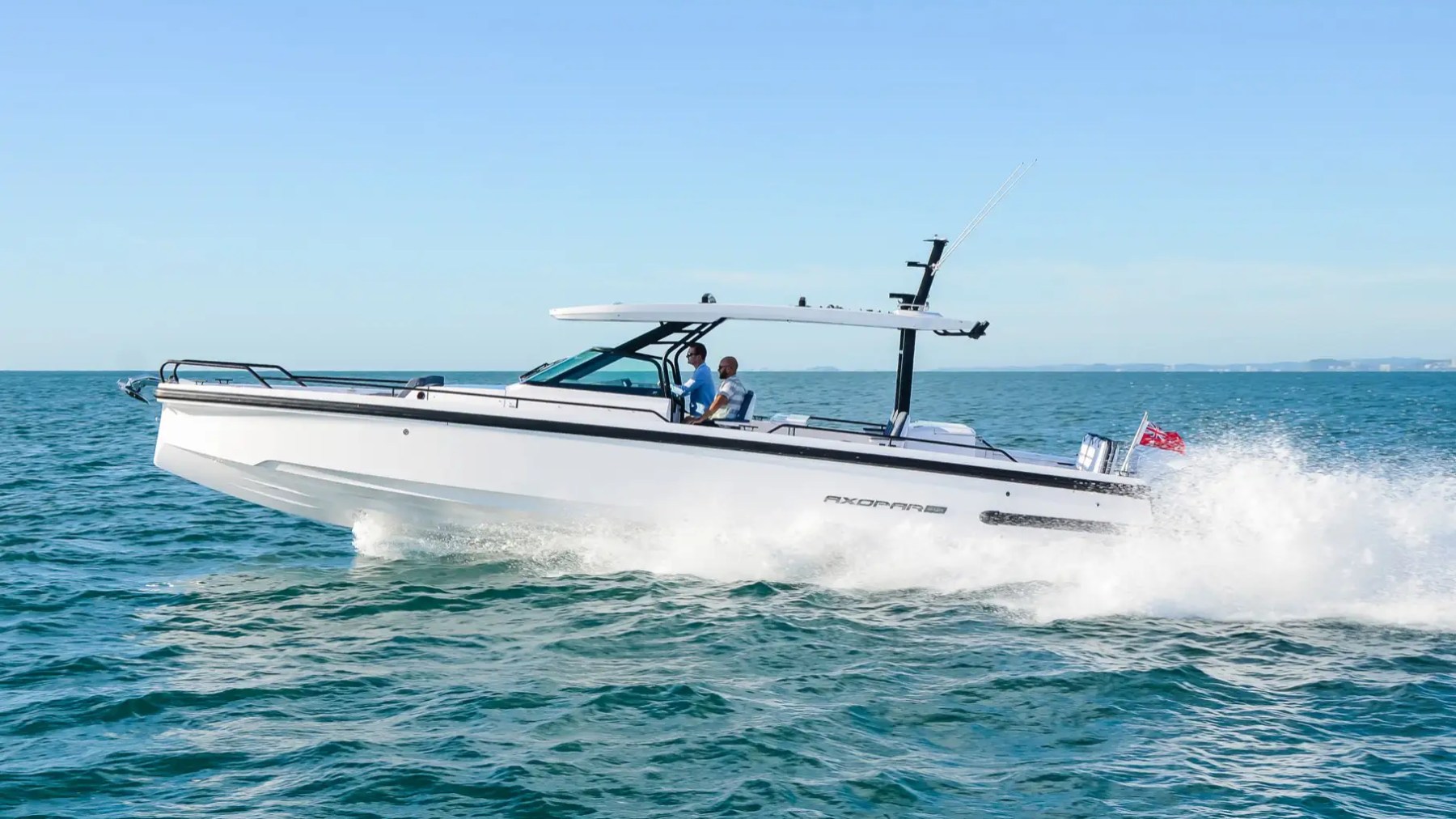 White motorboat speeding on the ocean with two people onboard under clear blue sky.