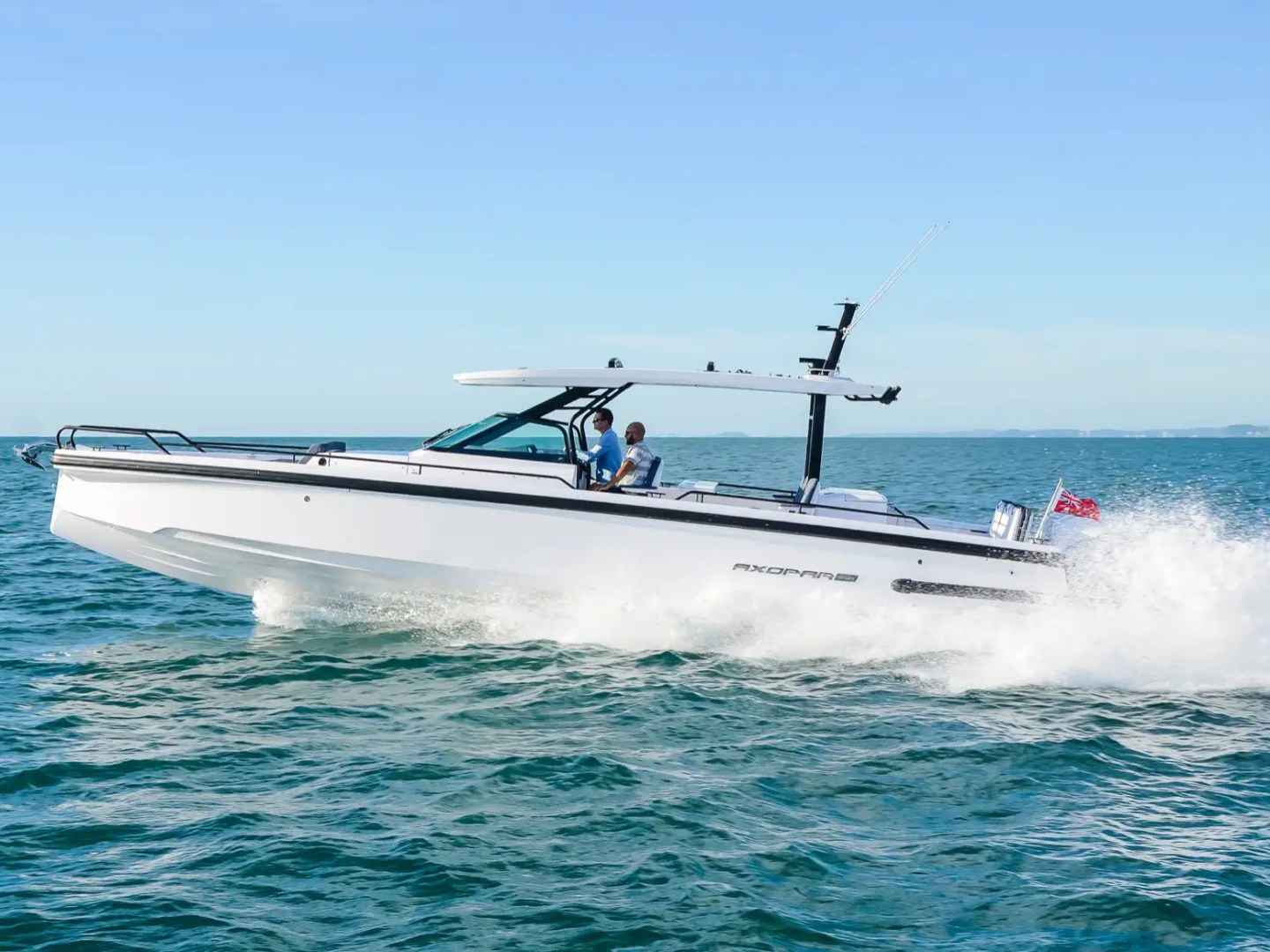 White motorboat speeding on the ocean with two people onboard under clear blue sky.