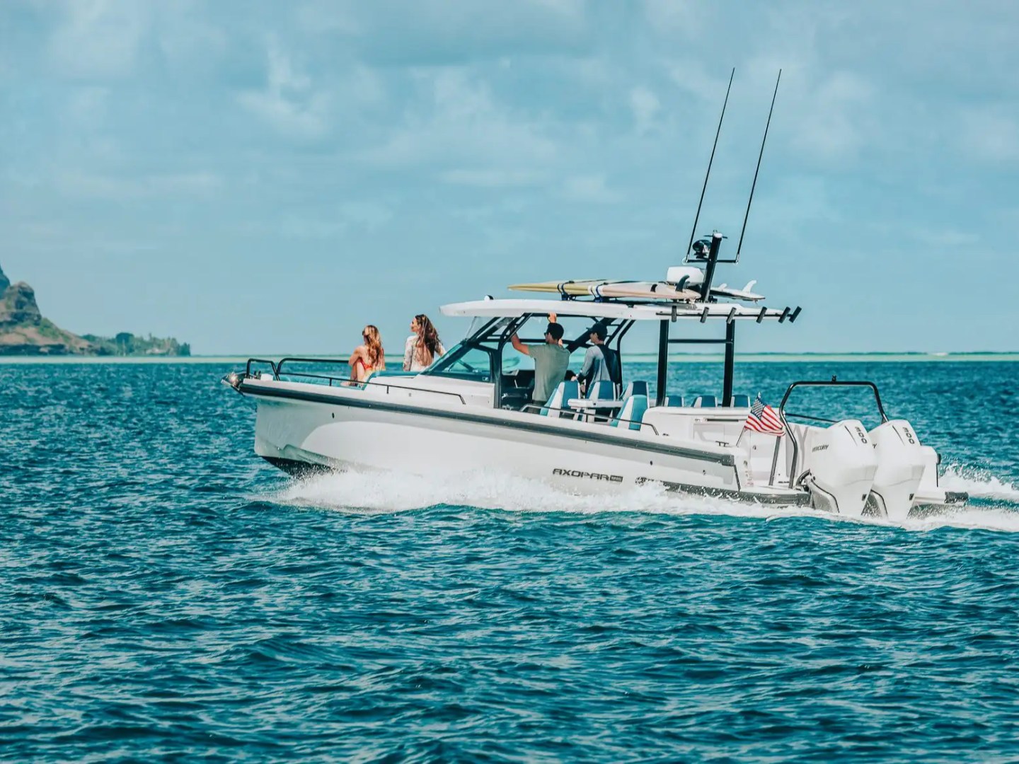 A white motorboat cruising with passengers on a calm ocean near a hilly coastline.