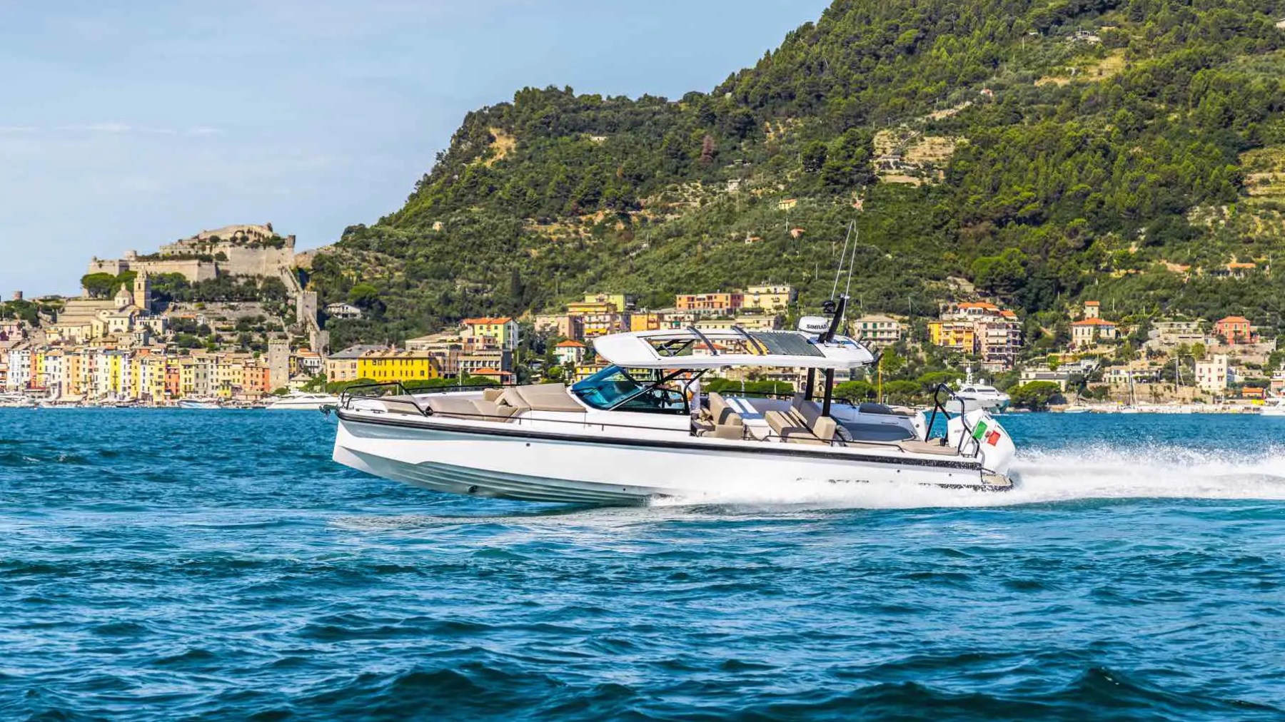 Speedboat on blue water with colorful town and green hills in the background.