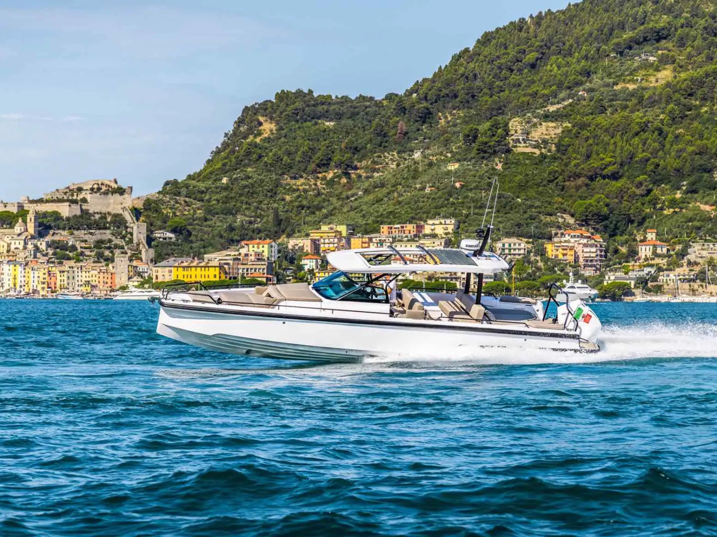 Speedboat on blue water with colorful town and green hills in the background.