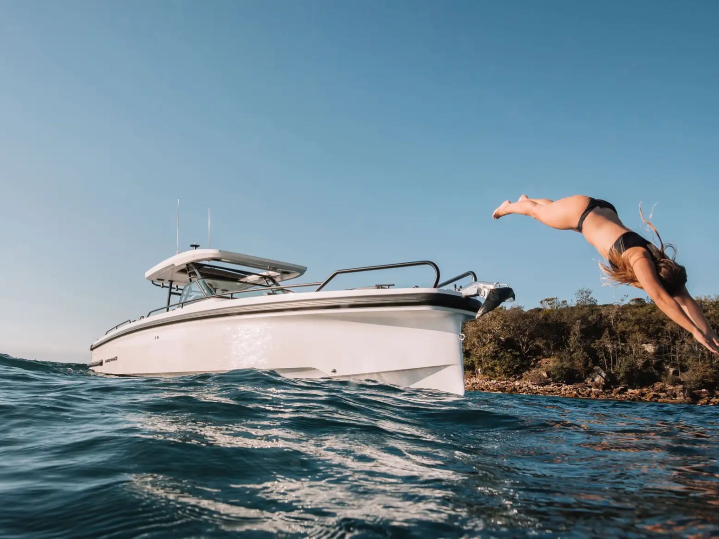 Person diving off a boat into the ocean with clear blue sky.