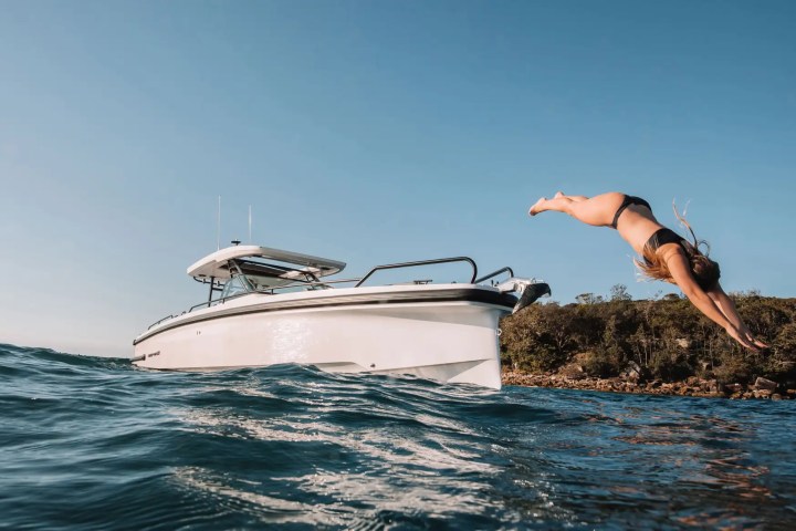 Person diving off a boat into the ocean with clear blue sky.