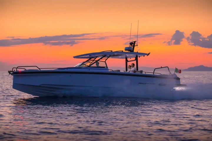 Boat cruising on ocean at sunset, with a couple onboard and Italian flag waving at the back.