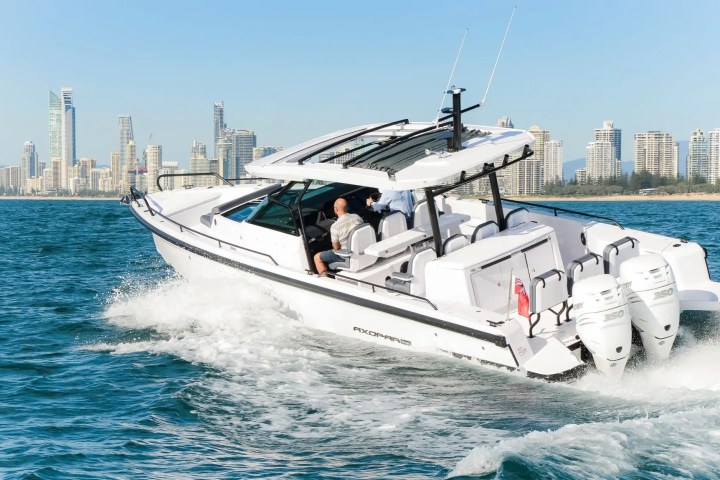 White motorboat speeding on water with city skyline in the background.
