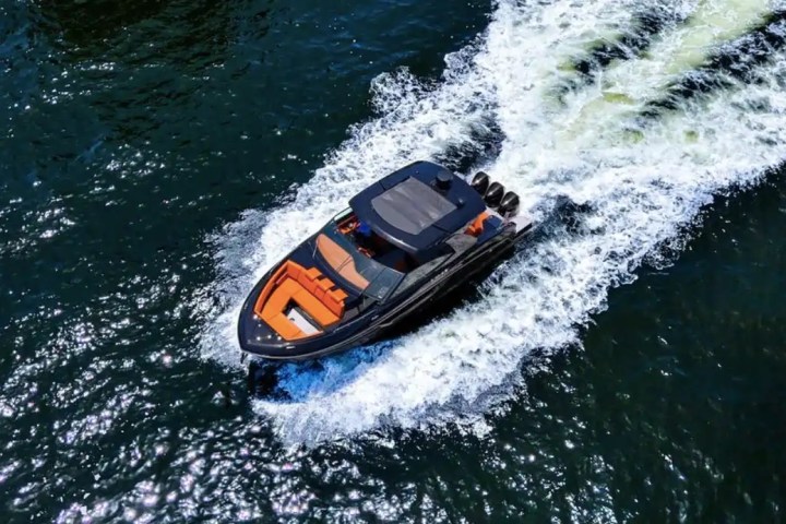 A luxury speedboat with orange seats speeding on a dark blue sea, leaving a frothy wake behind.