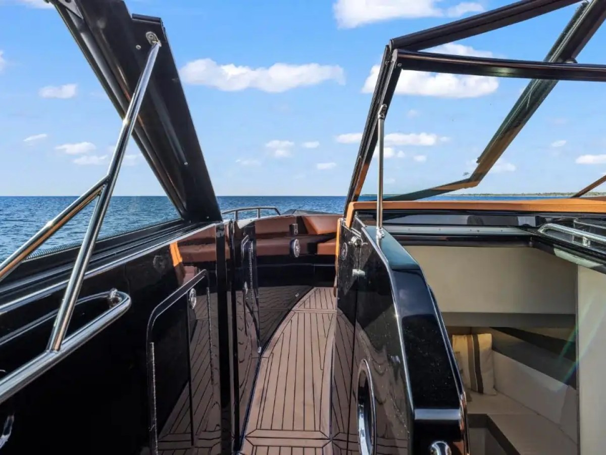 This 38 foot Cruisers Boat Rental features a walkthrough side deck leading to the open bow lounge, with expansive Gulf Coast water views and sleek black hull styling visible throughout the vessel.