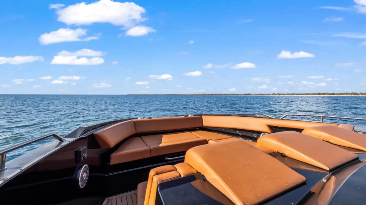 Luxury boat with tan seating cruising on a calm sea under a blue sky with scattered clouds.