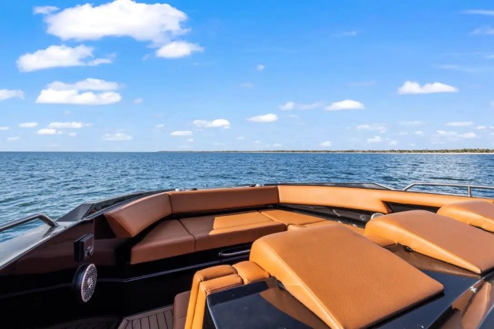Luxury boat with tan seating cruising on a calm sea under a blue sky with scattered clouds.