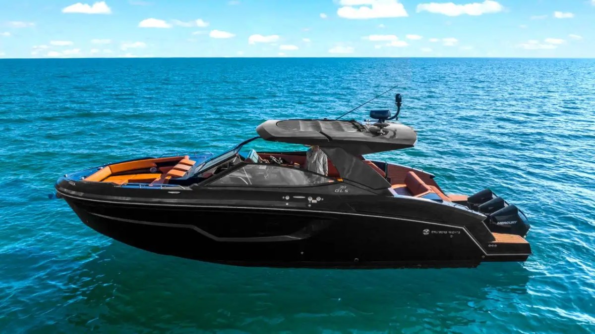 A sleek black motor yacht on a calm, sunny sea with a clear blue sky.