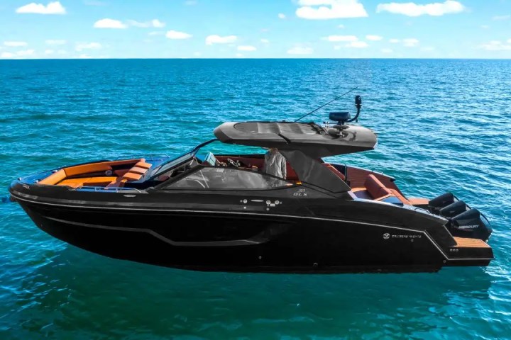 A sleek black motor yacht on a calm, sunny sea with a clear blue sky.