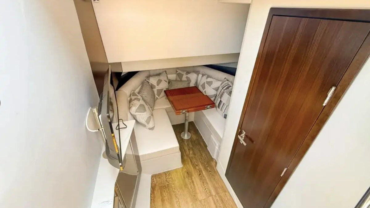 Small room with a wooden floor, wall-mounted TV, sofa with patterned cushions, and a small wooden table.