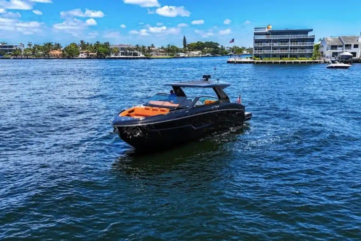 Sleek black yacht on blue water with buildings and trees in the background under a clear sky.