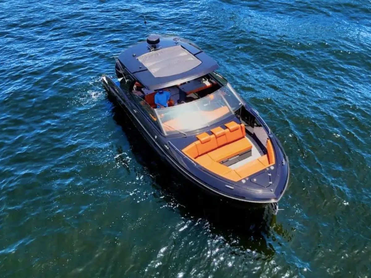 This 38 foot Cruisers Boat Rental is captured from an aerial view cruising Naples waterways, showcasing black hull styling, open bow lounge seating, and clear Southwest Florida waters.