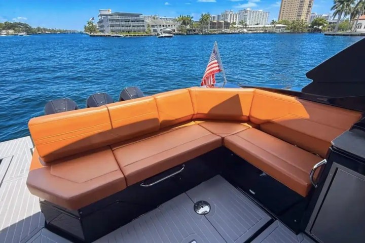Boat deck with orange seating, U.S. flag, and waterfront city view.