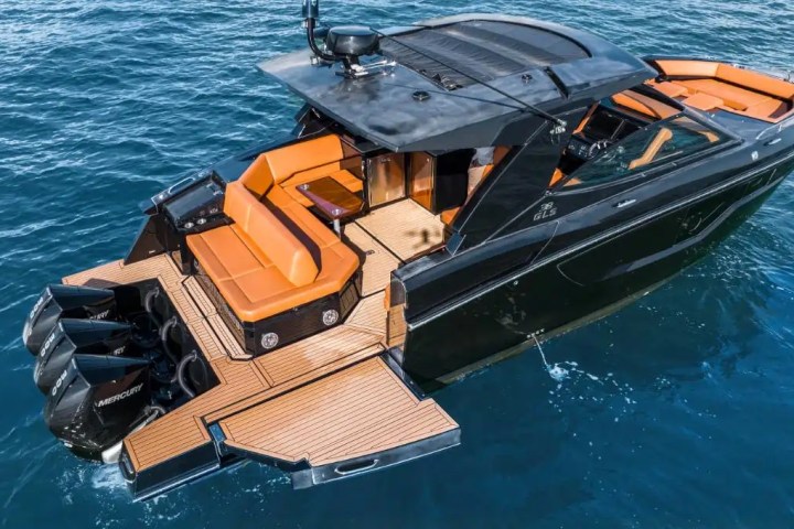 Luxury black boat with orange seating on blue water, view from above.