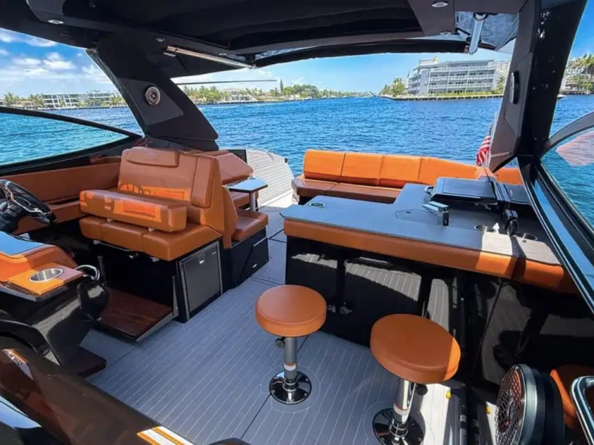 This 38 foot Cruisers Boat Rental features a modern cockpit lounge with premium seating, dining table, helm controls, and panoramic Naples waterfront views through the open-air cabin.