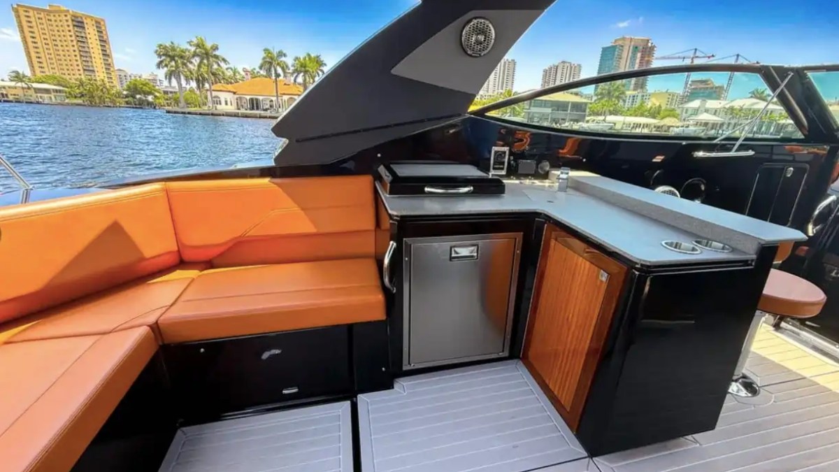 Luxury yacht deck with orange seating, kitchenette, and cityscape view.