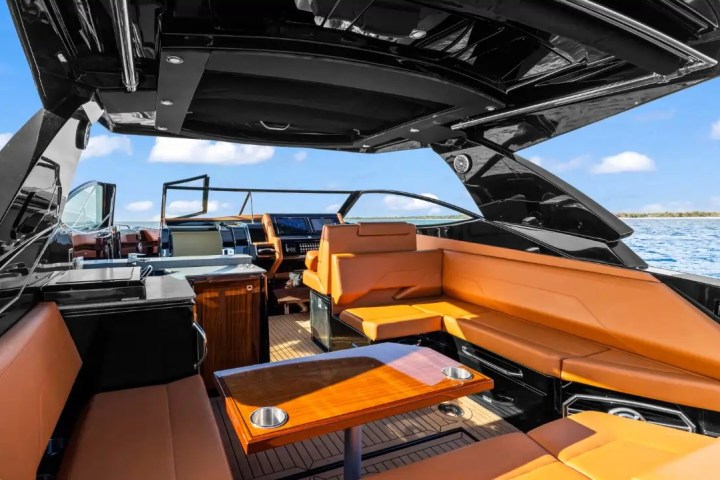 Luxury boat interior with tan leather seating and wooden table, open roof, on a sunny day at sea.