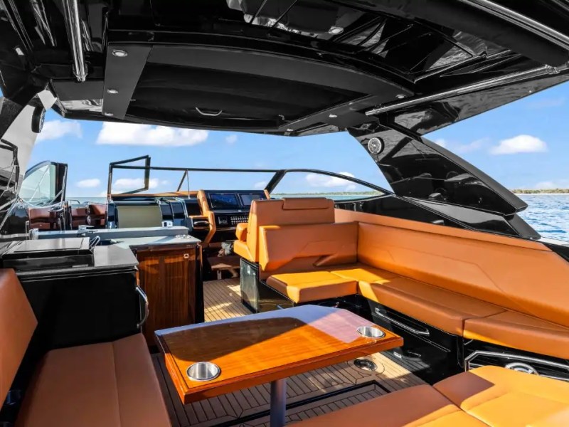 Luxury boat interior with tan leather seating and wooden table, open roof, on a sunny day at sea.