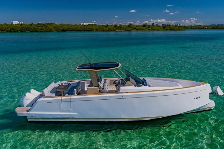 A white yacht floating on clear blue water under a sunny sky with distant greenery.