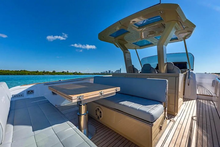 Luxury boat deck with seating area, table, and clear sky over calm waters.