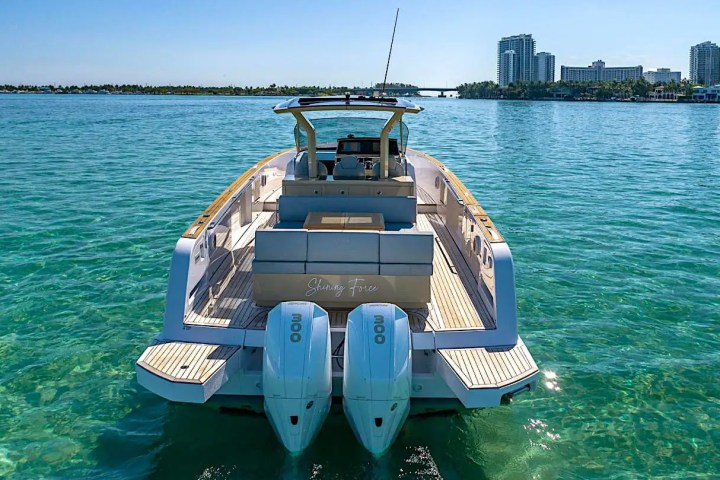 Rear view of a boat on clear turquoise water with city skyline in the background.