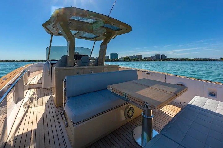 Boat deck with seating and table on a sunny day, city skyline in the background.