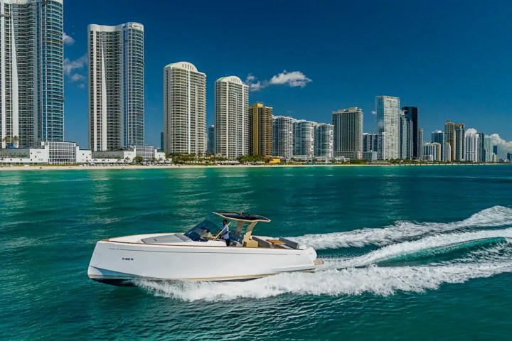 White yacht cruising on blue water with city skyscrapers in the background.