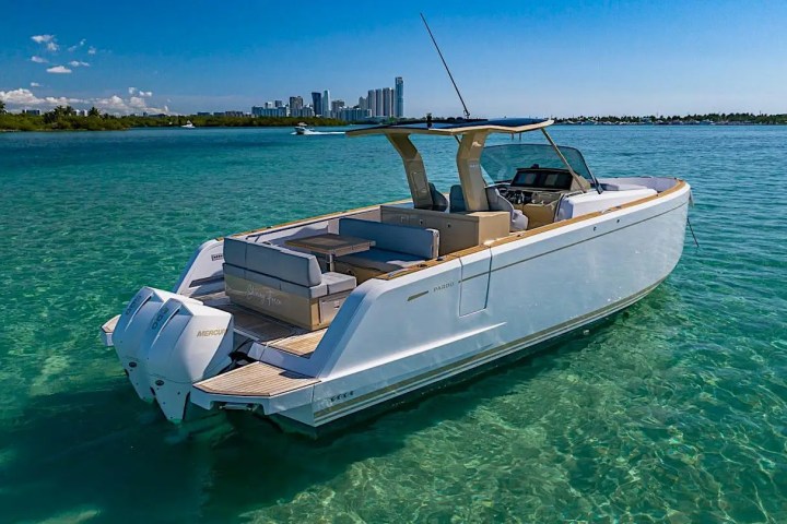 Luxury motorboat on clear turquoise water with city skyline in distance.